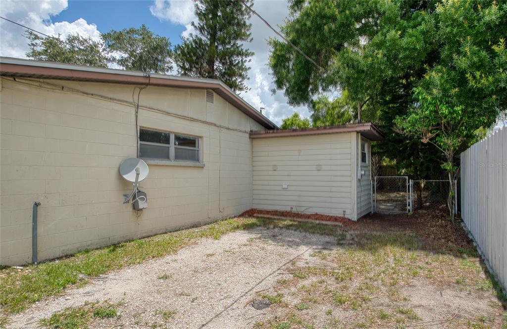 A gravel side yard sits beside a beige concrete block house with a satellite dish — 10205 N 29TH STREET, TAMPA, FL