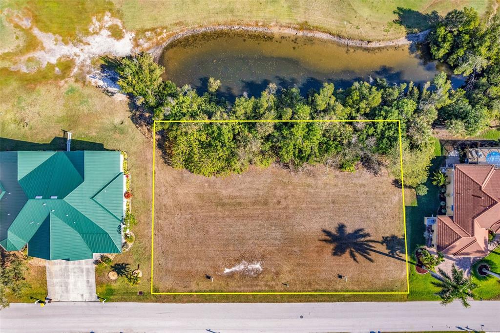 An aerial view shows a vacant, rectangular residential lot bordered by a pond and trees — 2316 PADRE ISLAND DRIVE, PUNTA GORDA, FL