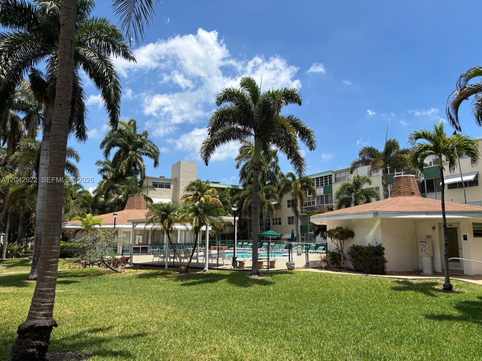 A swimming pool area with palm trees and a multi-story building under a blue sky — 1333 E Hallandale Beach Blvd # 134, Hallandale Beach FL 33009, HALLANDALE BEACH, FL