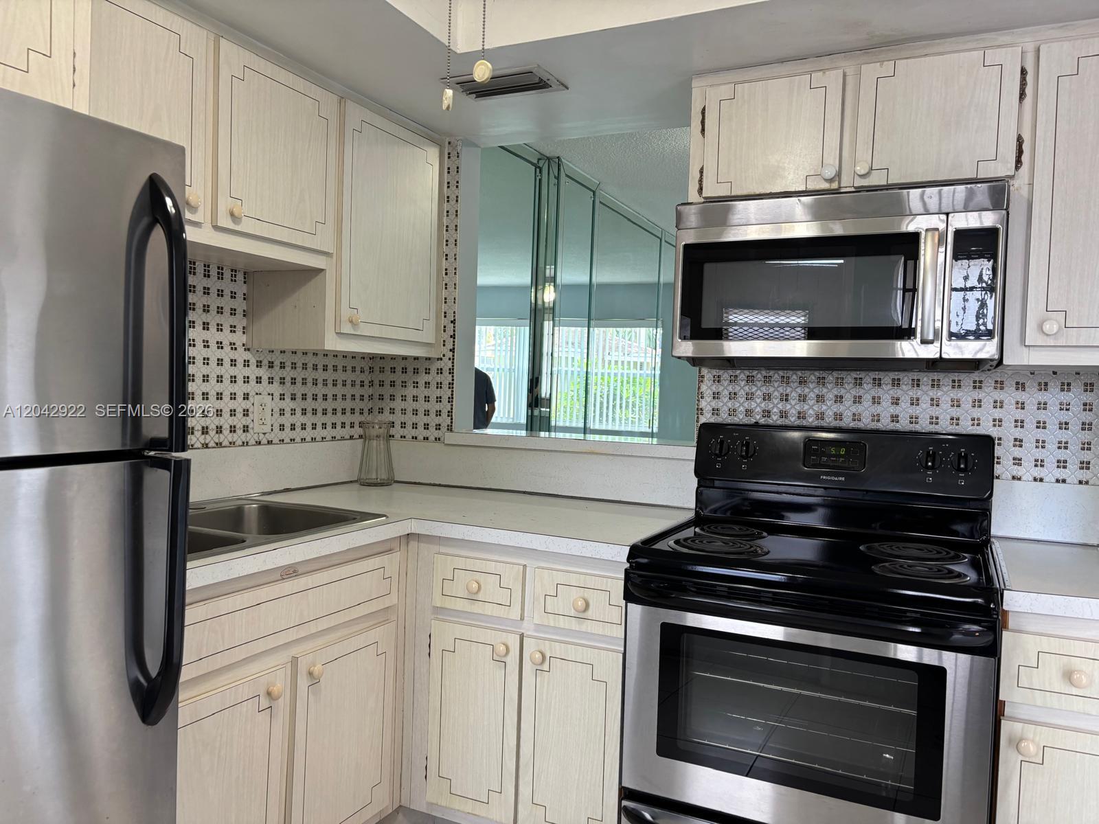 A kitchen features light wood cabinets, stainless steel appliances, and a patterned tile backsplash — 1333 E Hallandale Beach Blvd # 134, Hallandale Beach FL 33009, HALLANDALE BEACH, FL