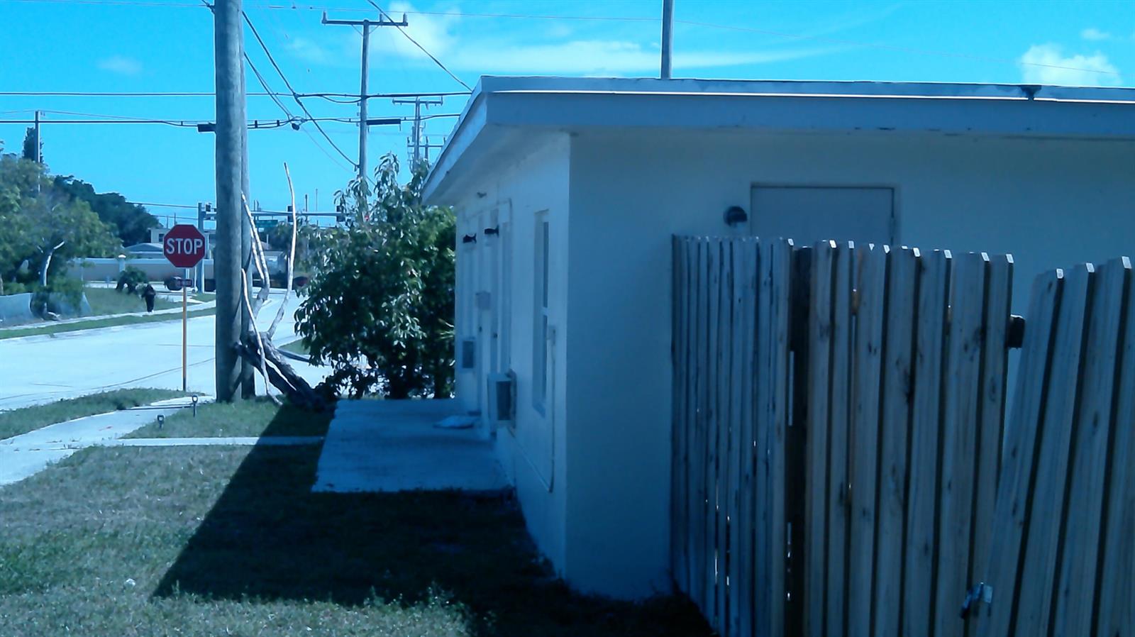 A white building exterior features a wooden fence, a concrete walkway, and a stop sign — 900 W 9th Street, Riviera Beach FL 33404, RIVIERA BEACH, FL
