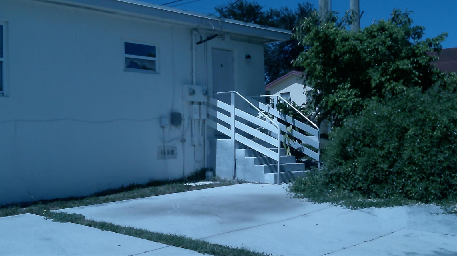 A white building exterior features a concrete staircase with white railings leading to a door — 900 W 9th Street, Riviera Beach FL 33404, RIVIERA BEACH, FL