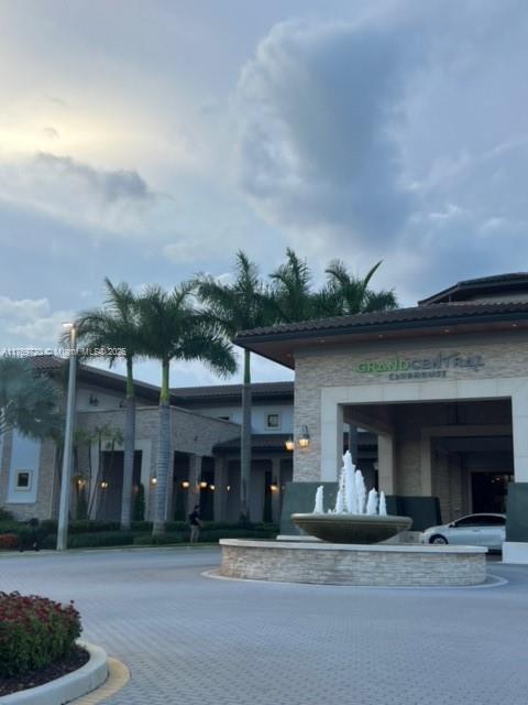 A stone clubhouse building features a circular fountain in the foreground and tall palm trees — 10630 NW 88th St # 103, Doral FL 33178, DORAL, FL