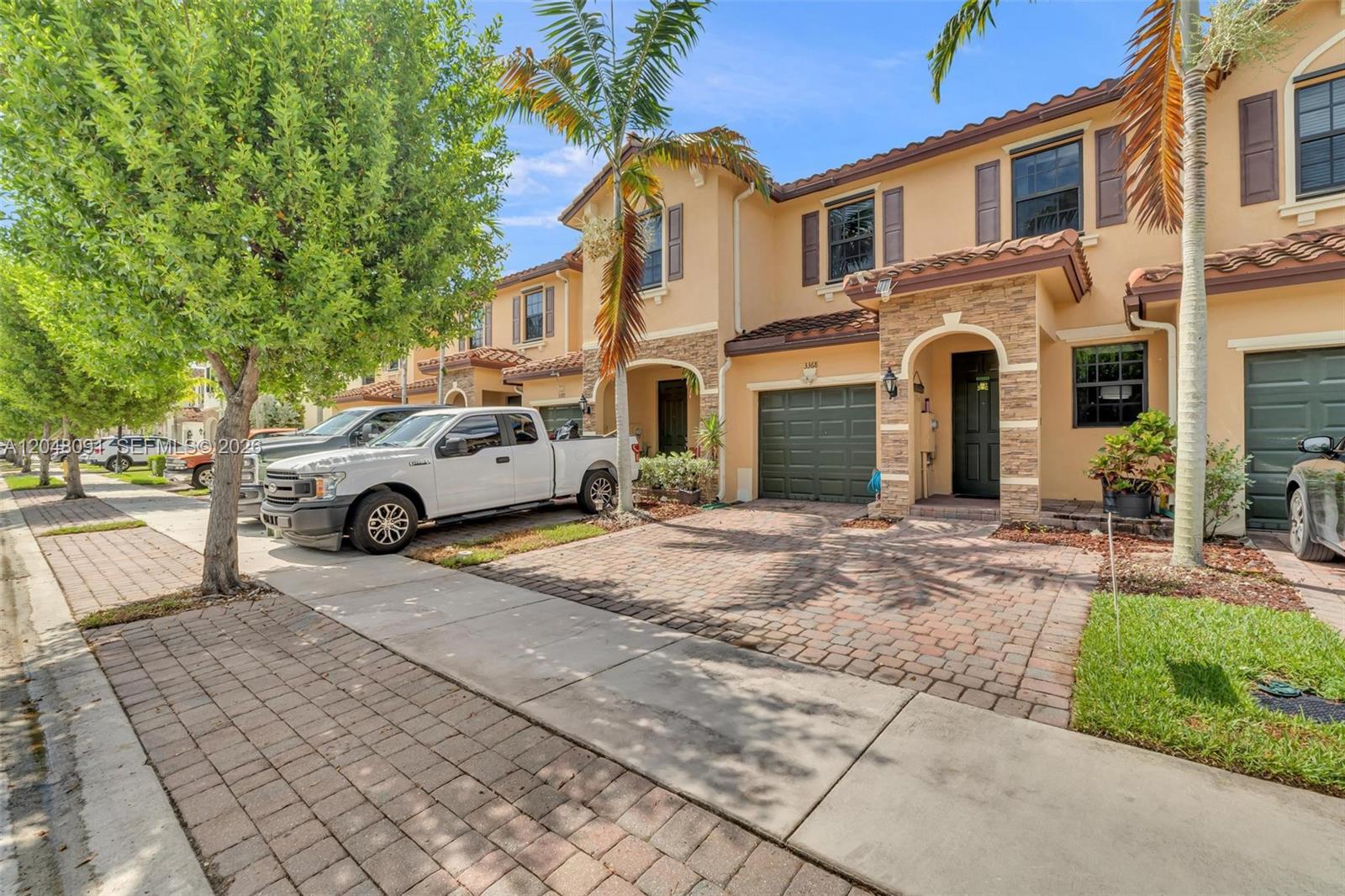 A street-level view of a two-story townhouse with a brick driveway and a garage — 3368 SE 1st St, Homestead FL 33033, HOMESTEAD, FL
