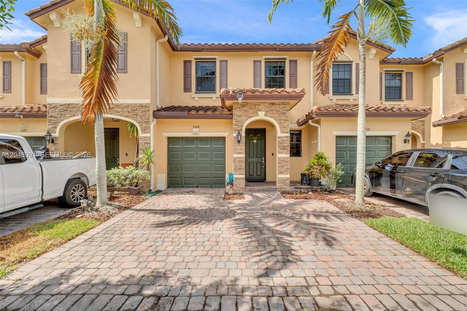 A two-story townhouse with a stone-accented facade, a brick driveway, and two green garage doors — 3368 SE 1st St, Homestead FL 33033, HOMESTEAD, FL