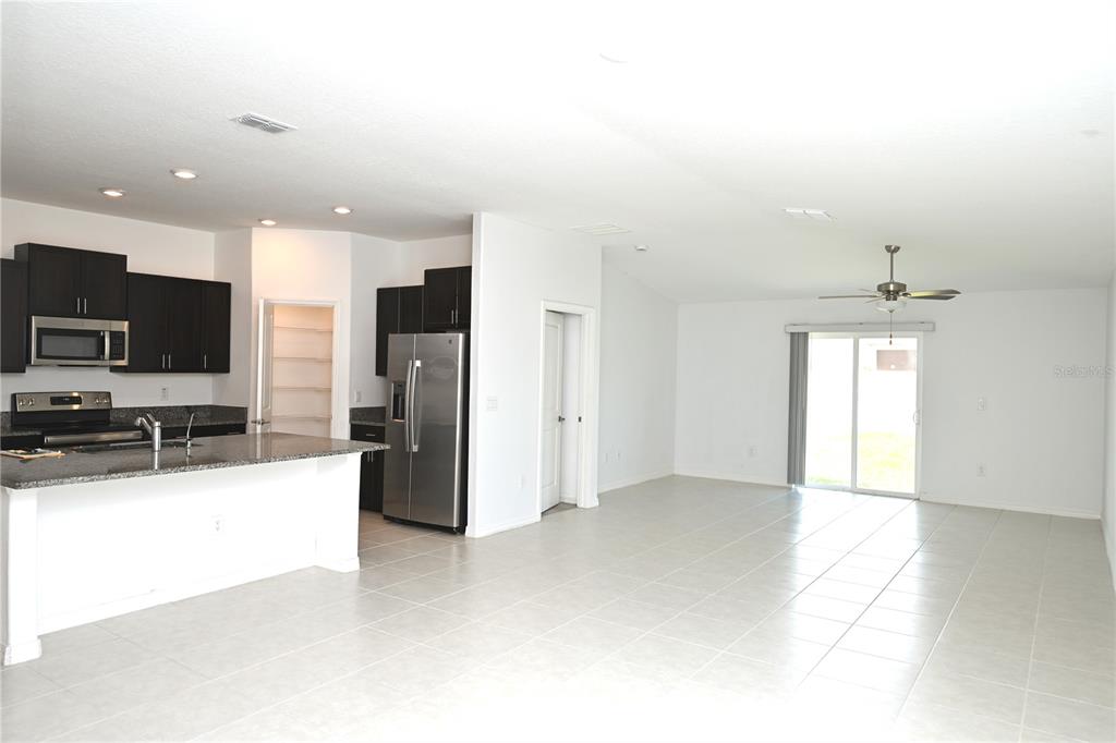 A bright, empty room with white walls, tiled floors, a ceiling fan, and sliding glass doors — 2674 RED EGRET DRIVE, BARTOW, FL