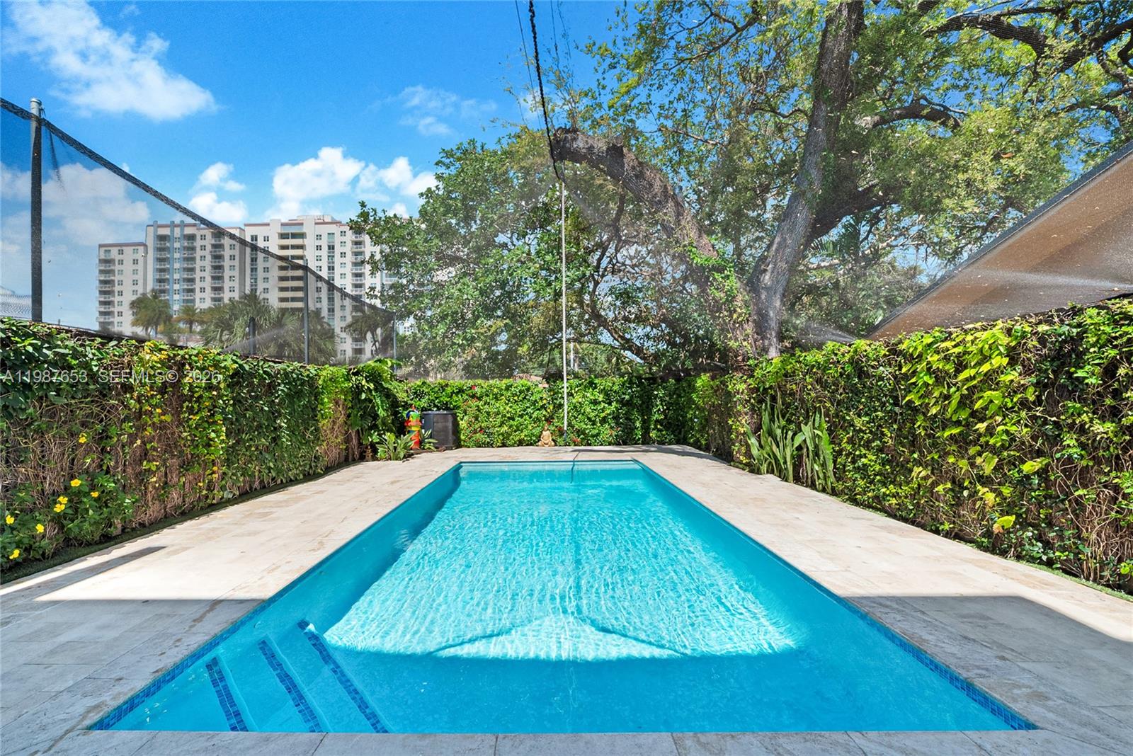 A rectangular swimming pool is surrounded by stone decking and enclosed by a privacy hedge — 2943 SW 23rd St, Miami FL 33145, MIAMI, FL