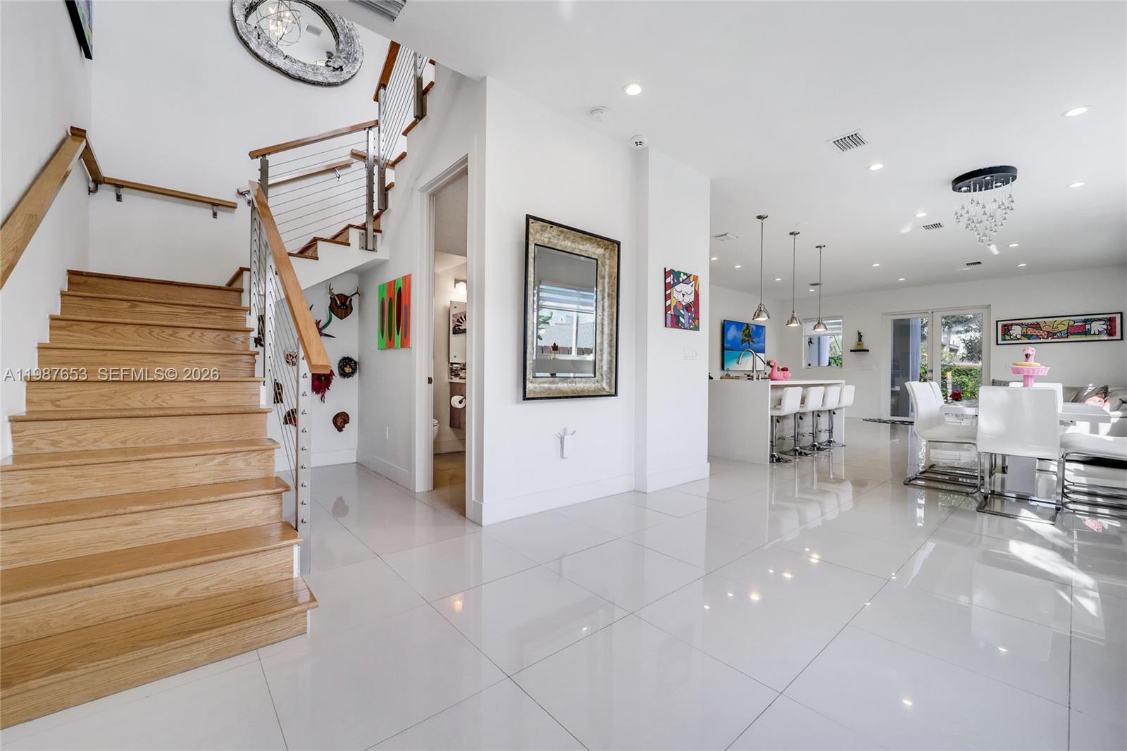 A modern open-concept interior features a wooden staircase, white tile flooring, and a kitchen island — 2943 SW 23rd St, Miami FL 33145, MIAMI, FL