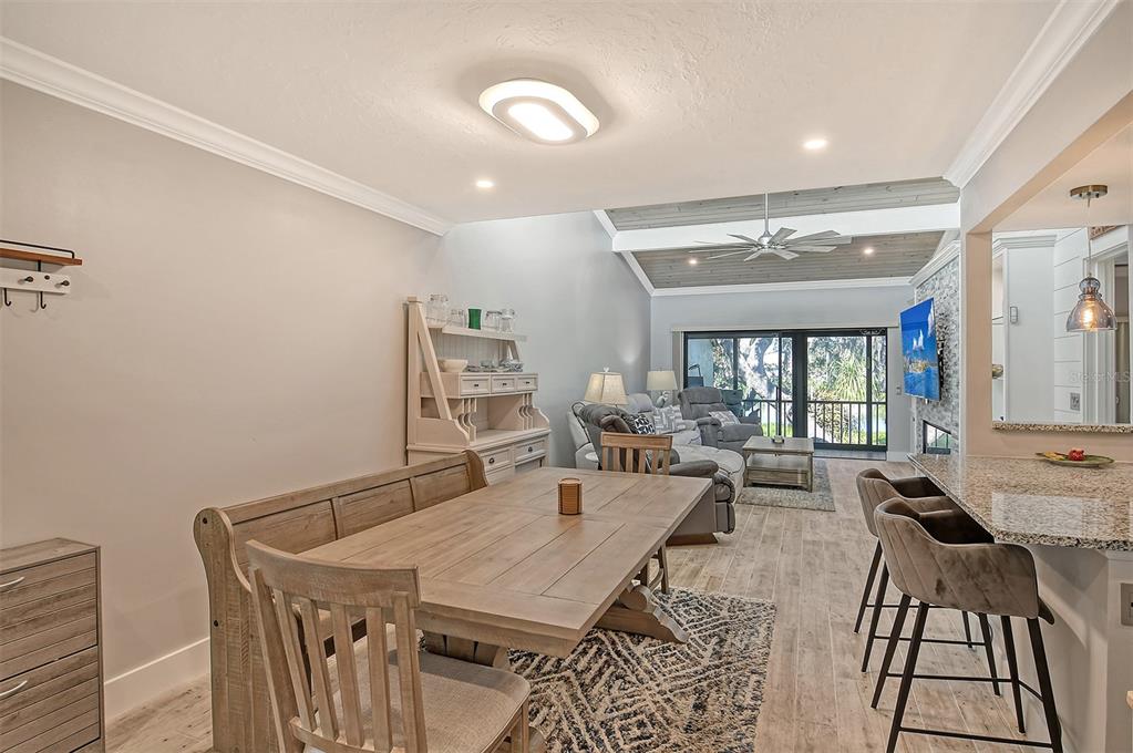 An open-concept dining and living area features a wooden table, breakfast bar, and vaulted ceilings — 1601 BAYHOUSE POINT DRIVE UNIT BA206, SARASOTA, FL