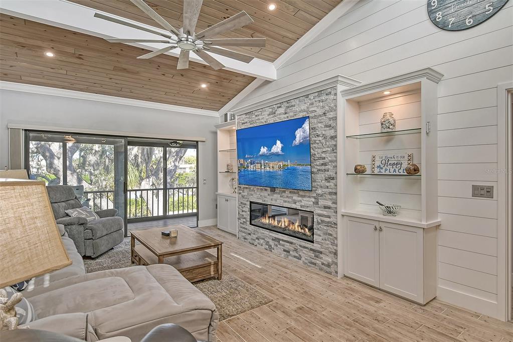 A living room features a stone fireplace, built-in shelving, a vaulted wood ceiling, and sliding doors — 1601 BAYHOUSE POINT DRIVE UNIT BA206, SARASOTA, FL
