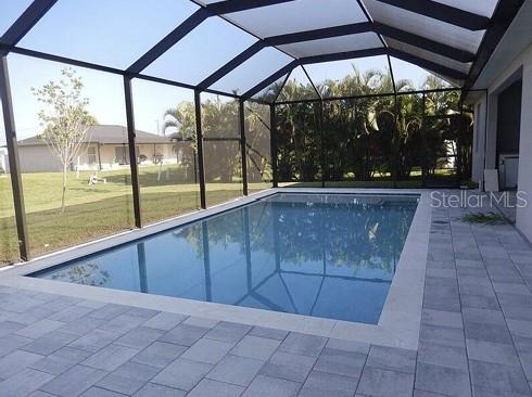 A rectangular swimming pool is enclosed by a screened lanai with light-colored stone pavers — 1306 NE 2ND AVENUE, CAPE CORAL, FL