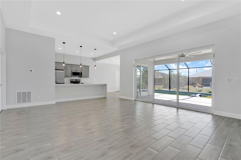 An open-concept living area with light wood-look tile floors, a kitchen, and sliding glass doors — 1306 NE 2ND AVENUE, CAPE CORAL, FL