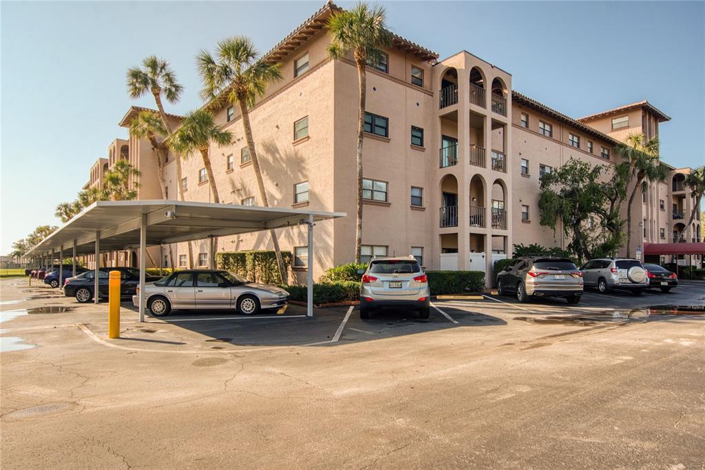 An exterior view of a multi-story apartment building with a covered parking area and cars — 6150 GULFPORT BOULEVARD S UNIT 413, GULFPORT, FL