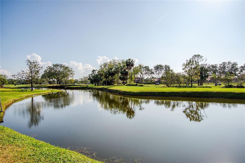 A calm pond reflects the surrounding green golf course, trees, and blue sky — 6150 GULFPORT BOULEVARD S UNIT 413, GULFPORT, FL
