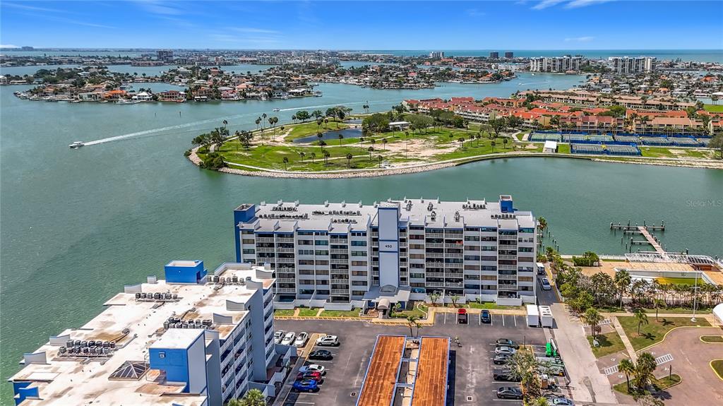 An aerial view shows a multi-story apartment building situated on a waterfront peninsula — 450 TREASURE ISLAND CAUSEWAY UNIT 111, TREASURE ISLAND, FL