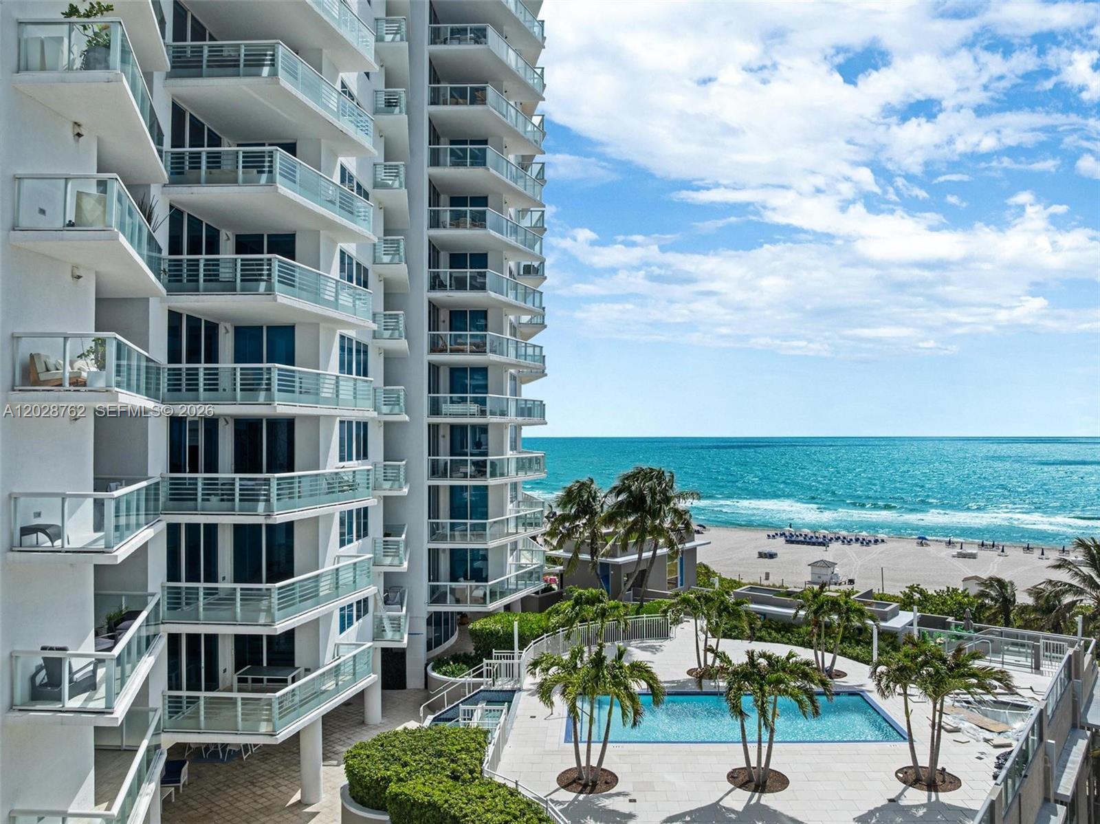 A high-rise residential building overlooks a swimming pool, palm trees, and the ocean beach — 3801 Collins Ave # 703, Miami Beach FL 33140, MIAMI BEACH, FL
