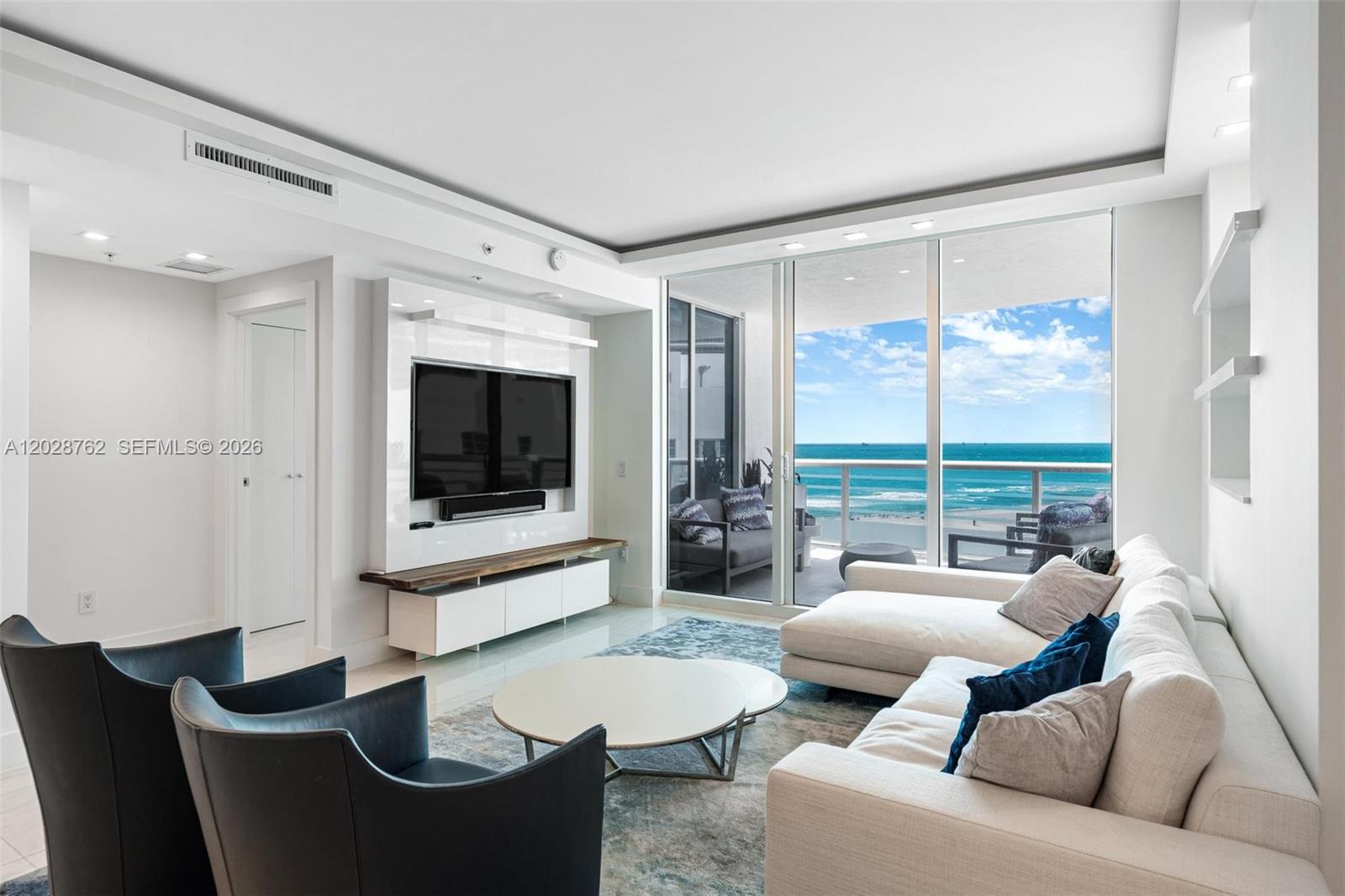 A modern living room features a white media wall, sectional sofa, and floor-to-ceiling ocean views — 3801 Collins Ave # 703, Miami Beach FL 33140, MIAMI BEACH, FL