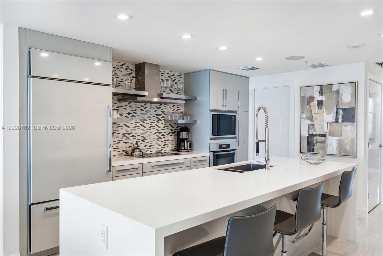 A modern kitchen features a white island, stainless steel appliances, and a mosaic tile backsplash — 3801 Collins Ave # 703, Miami Beach FL 33140, MIAMI BEACH, FL