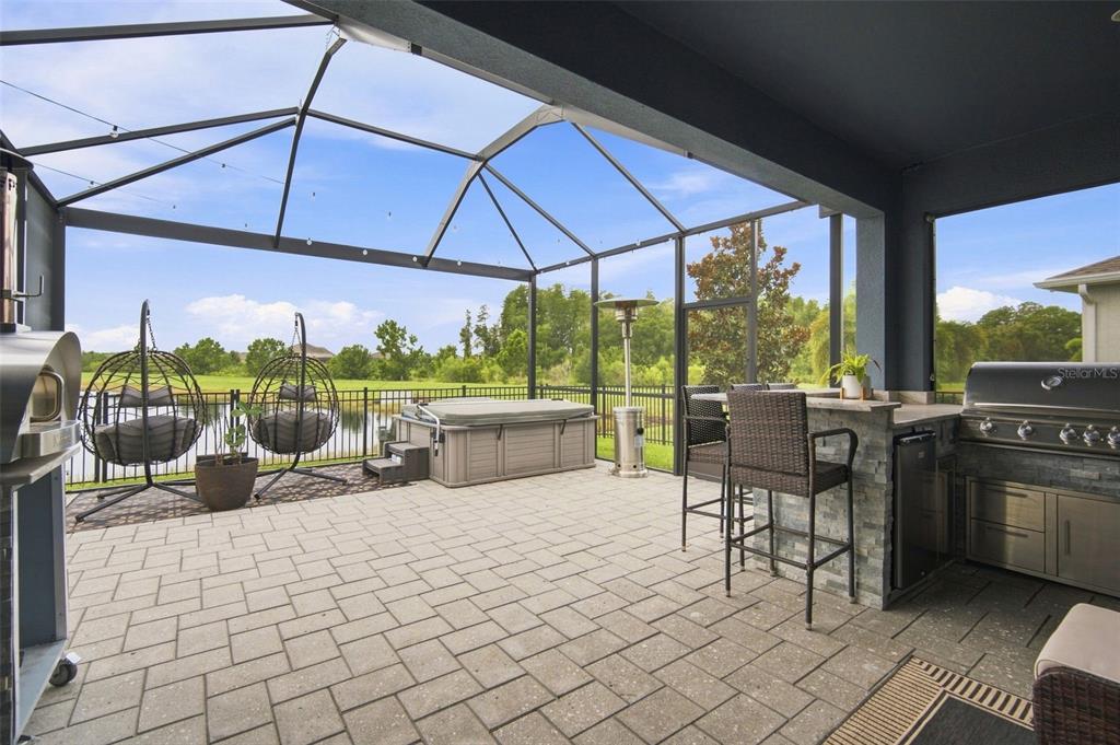 A screened-in patio features a hot tub, outdoor kitchen, and hanging chairs overlooking a pond — 5306 SILVER SUN DRIVE, APOLLO BEACH, FL