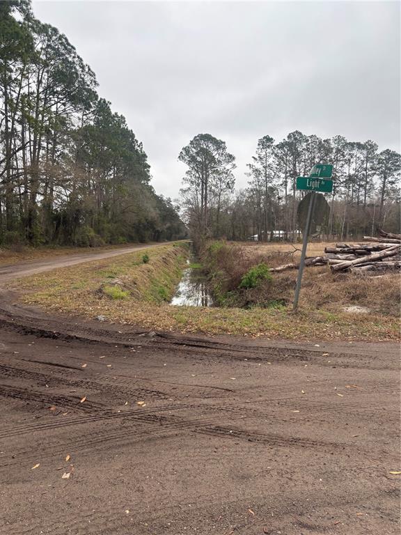 A dirt road intersection features a drainage ditch, a street sign, and a wood pile — 9600 LIGHT AVENUE, HASTINGS, FL