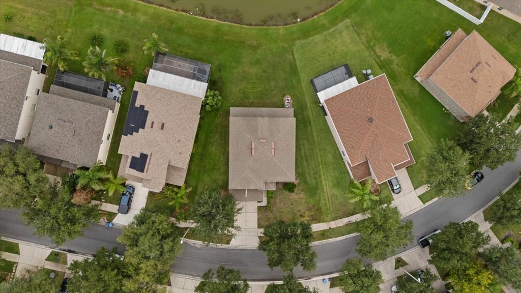 An aerial view shows three suburban houses with driveways and backyards near a small pond — 10616 LIBERTY BELL DRIVE, TAMPA, FL