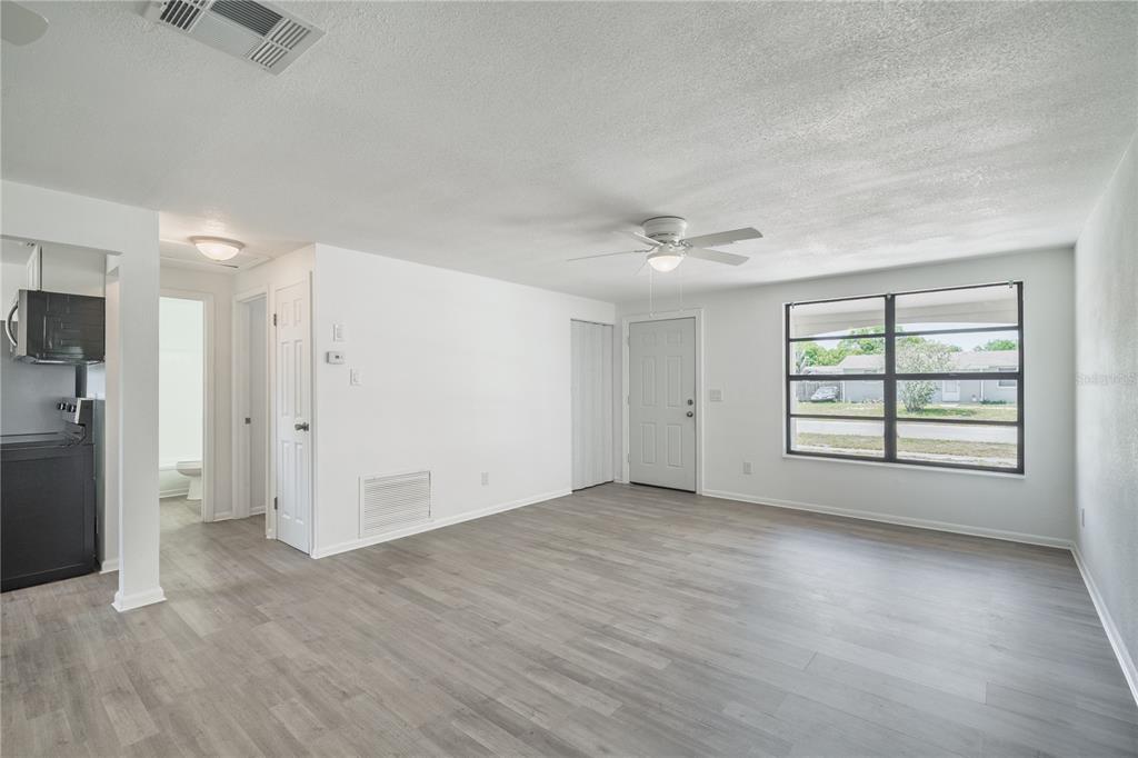 A bright living room with light gray wood-look flooring, white walls, and a ceiling fan — 2919 KEESLER STREET, DELTONA, FL