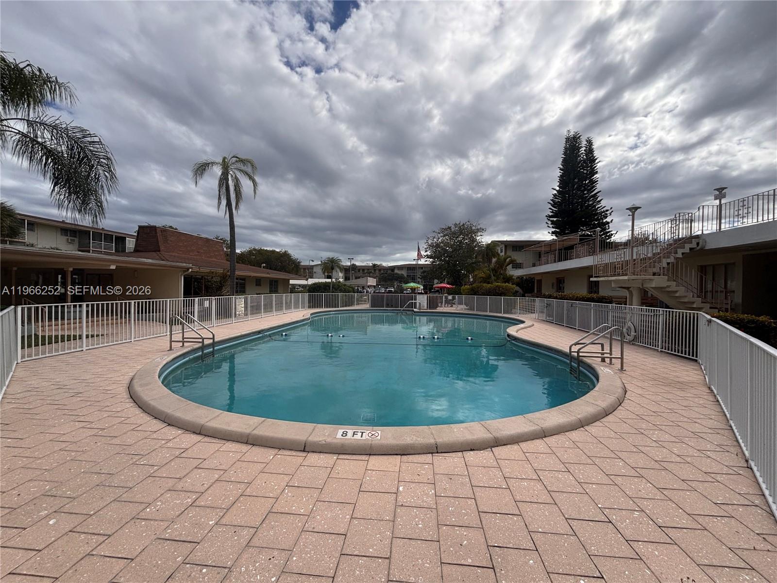 An outdoor swimming pool is surrounded by a paved deck and white metal fencing — 16900 NE 14th Ave # 111, Miami FL 33162, MIAMI, FL