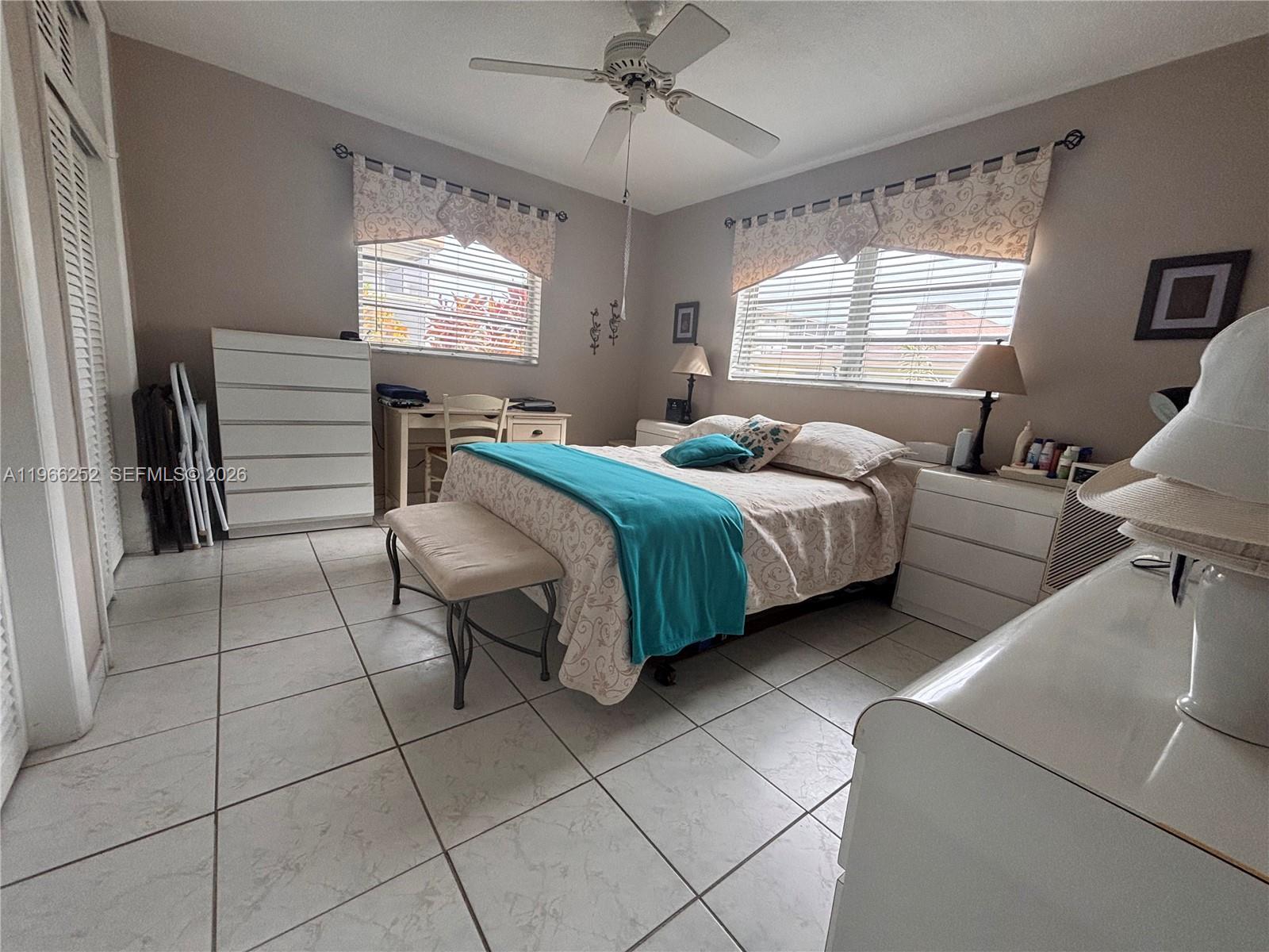 A bedroom features a bed with a teal throw, tile flooring, and a ceiling fan — 16900 NE 14th Ave # 111, Miami FL 33162, MIAMI, FL