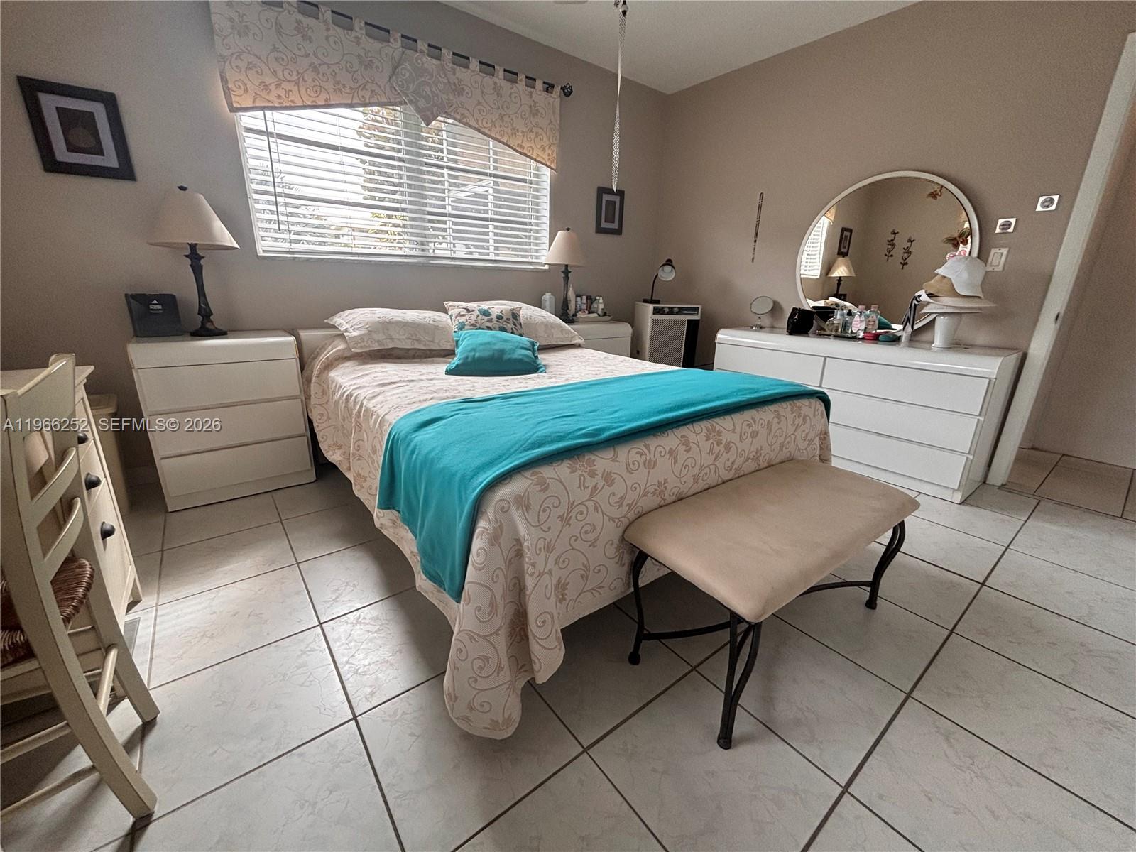 A bedroom features a bed with a teal throw, white furniture, and tiled flooring — 16900 NE 14th Ave # 111, Miami FL 33162, MIAMI, FL