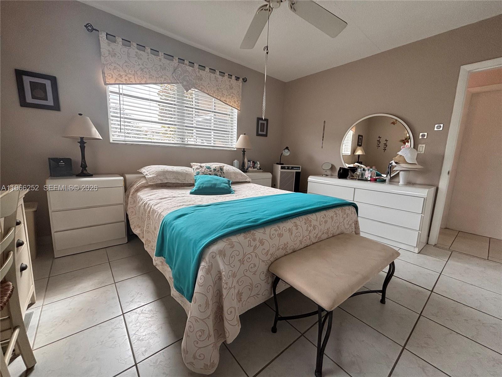 A bedroom features a bed with a teal throw, white furniture, and tile flooring — 16900 NE 14th Ave # 111, Miami FL 33162, MIAMI, FL
