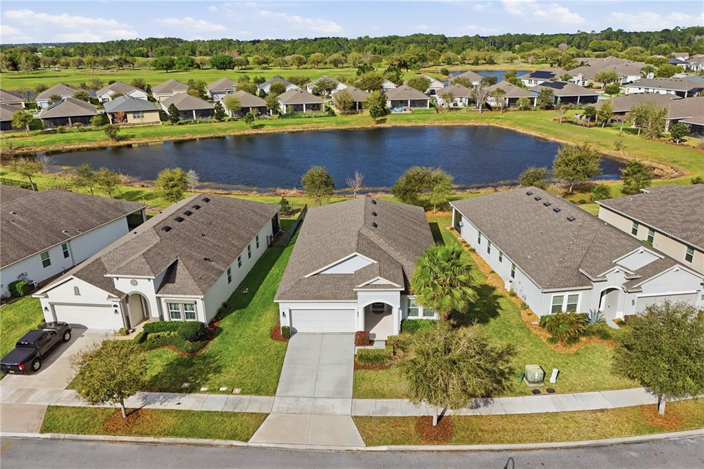 An aerial view shows three suburban houses with gray roofs situated along a small lake — 3383 SAGEBRUSH STREET, HARMONY, FL