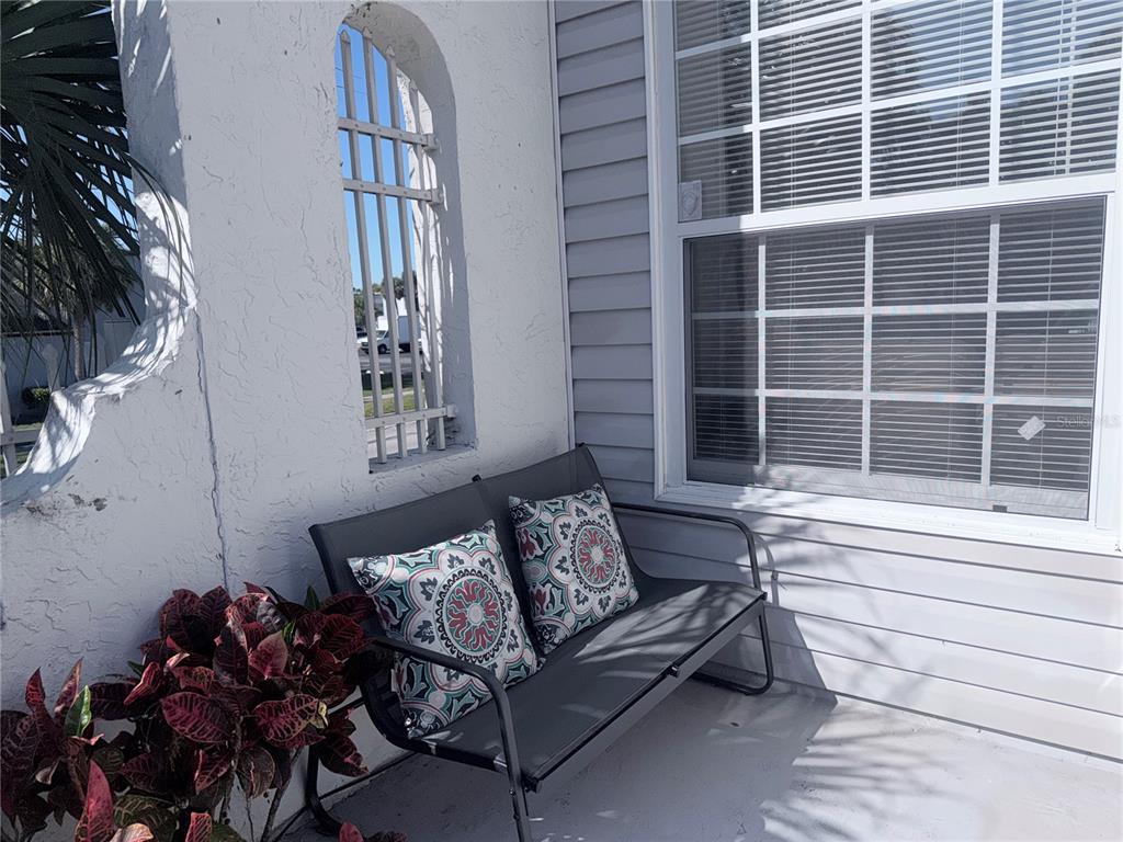 A gray metal bench with patterned pillows sits on a patio near a window — 7321 JACKSON SPRINGS ROAD, TAMPA, FL