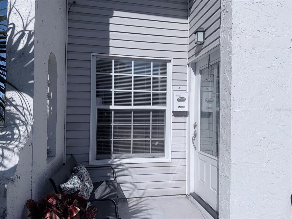 A white-sided entryway features a window with blinds, a front door, and a small bench — 7321 JACKSON SPRINGS ROAD, TAMPA, FL