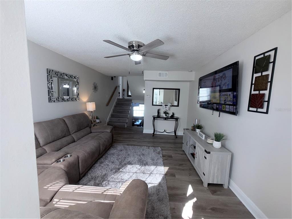 A living room features a gray sectional sofa, wood-look flooring, and a wall-mounted television — 7321 JACKSON SPRINGS ROAD, TAMPA, FL