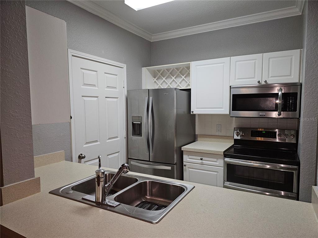 A kitchen features stainless steel appliances, white cabinets, and a double-basin sink on a countertop — 1216 S MISSOURI AVENUE UNIT 202, CLEARWATER, FL