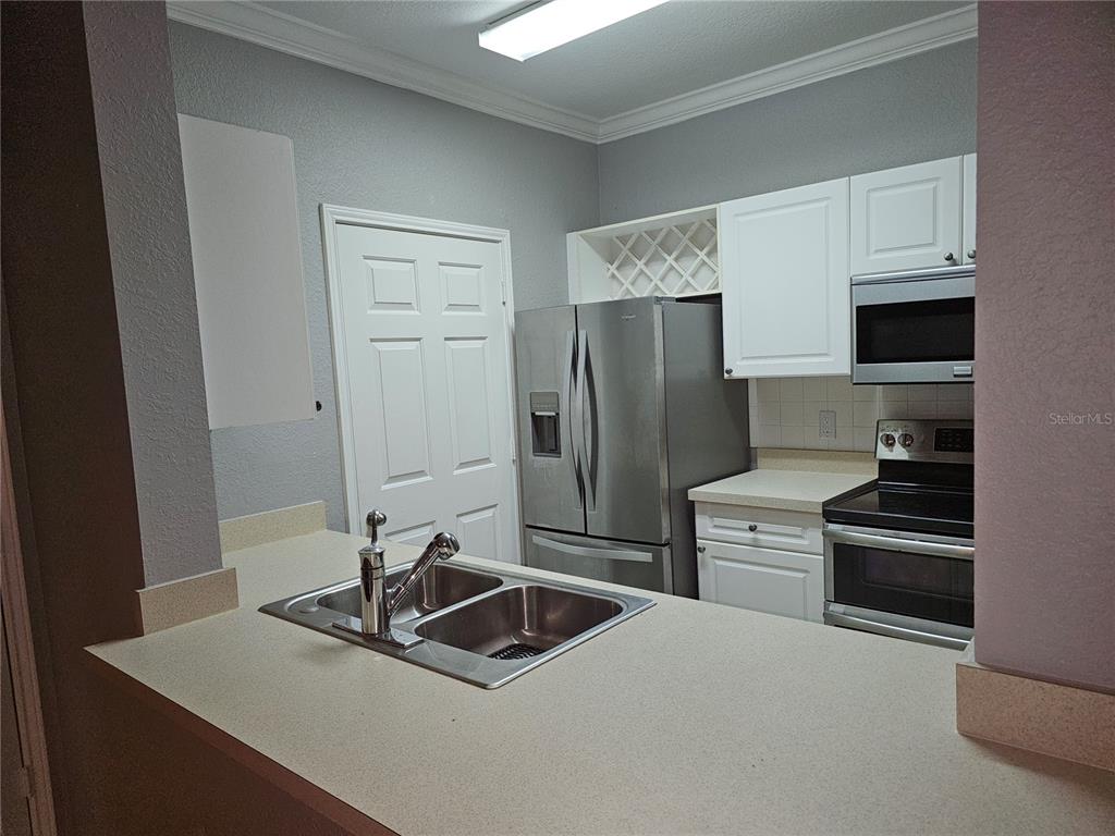 A kitchen features white cabinets, stainless steel appliances, and a double-basin sink on the counter — 1216 S MISSOURI AVENUE UNIT 202, CLEARWATER, FL
