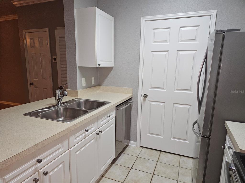 A kitchen features white cabinets, a stainless steel sink, a dishwasher, and a refrigerator — 1216 S MISSOURI AVENUE UNIT 202, CLEARWATER, FL