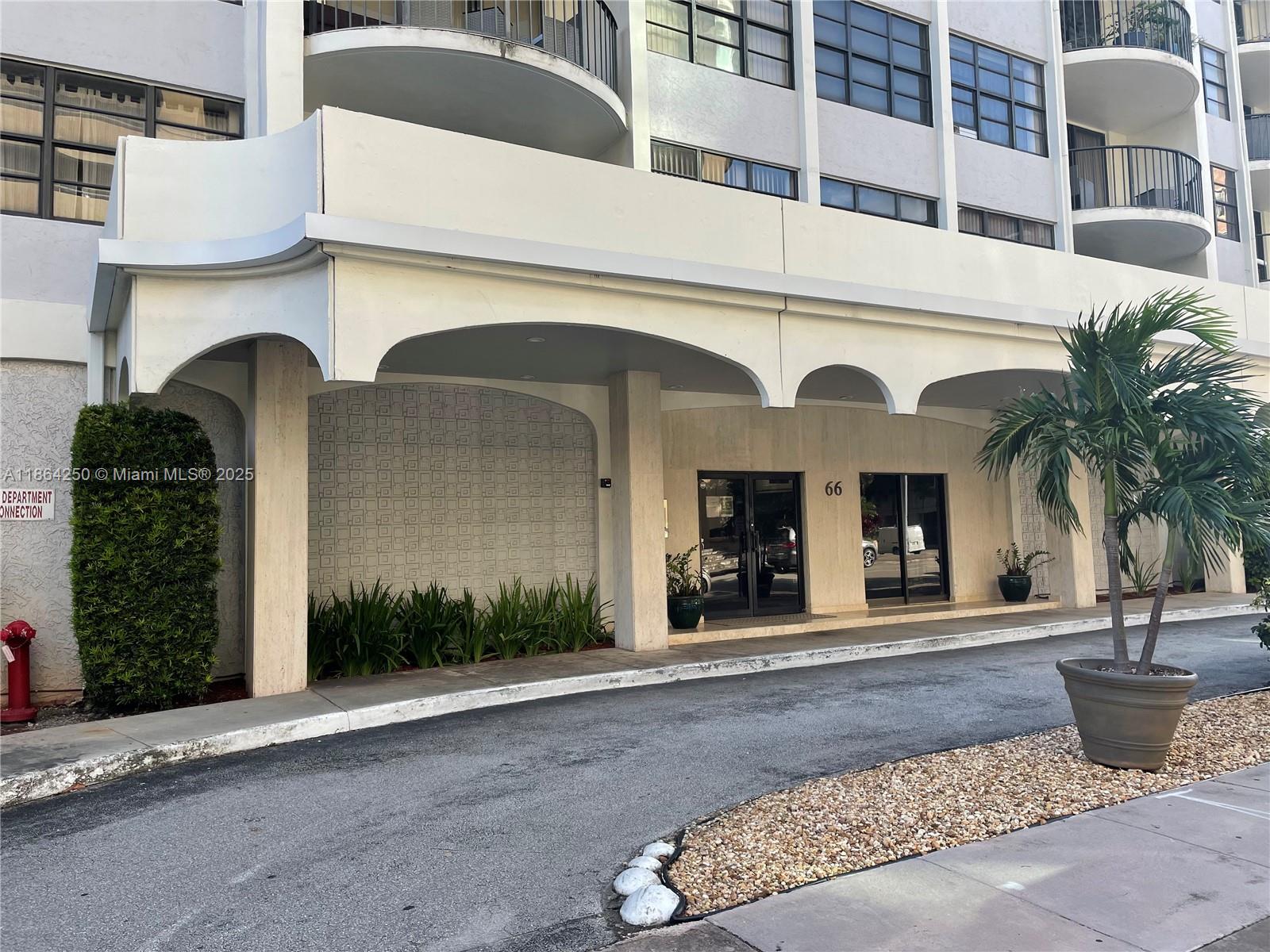The exterior of a multi-story building features a covered entrance with arched architectural details — 66 Valencia Ave, Coral Gables FL 33134, CORAL GABLES, FL