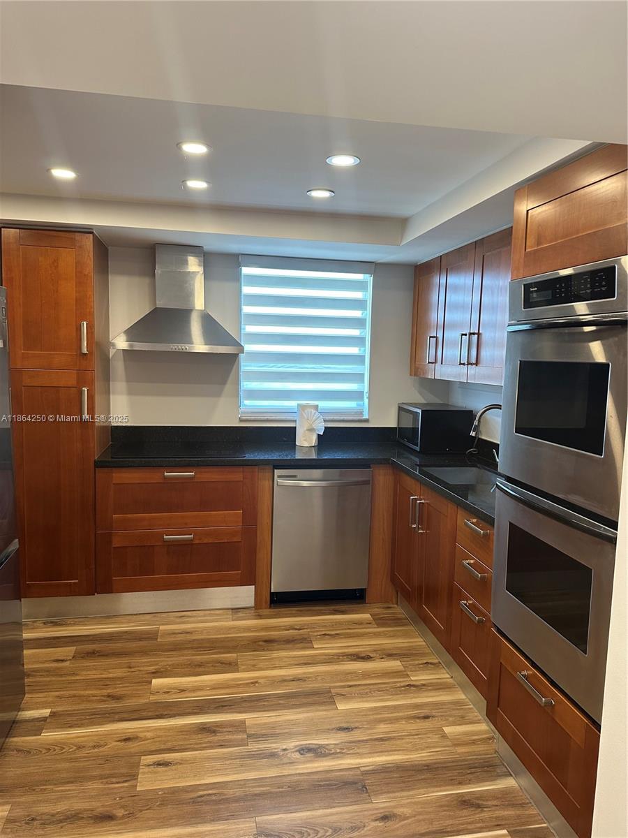 A kitchen features wood cabinets, stainless steel appliances, black countertops, and wood-look flooring — 66 Valencia Ave, Coral Gables FL 33134, CORAL GABLES, FL