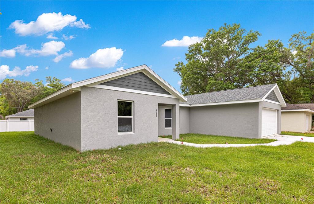 A single-story gray house with a white garage door and a grassy front yard — 8276 SE 158TH STREET, SUMMERFIELD, FL