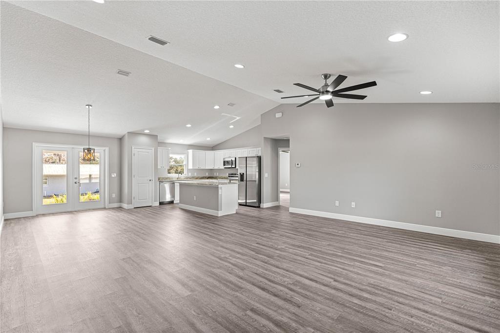 An open-concept living area features gray wood-look flooring, a kitchen with white cabinets, and vaulted ceilings — 8276 SE 158TH STREET, SUMMERFIELD, FL
