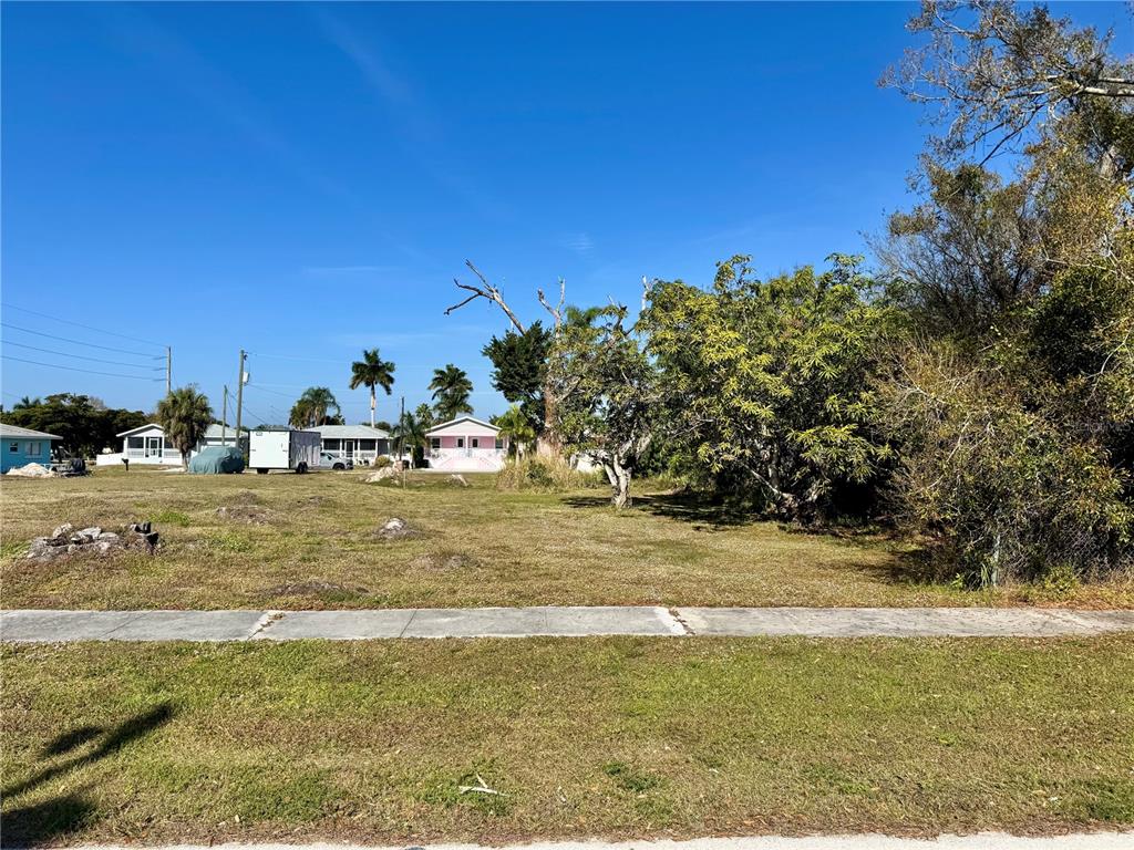 A vacant, grassy residential lot features a sidewalk in the foreground and distant houses — 623 FITZHUGH AVENUE, PUNTA GORDA, FL