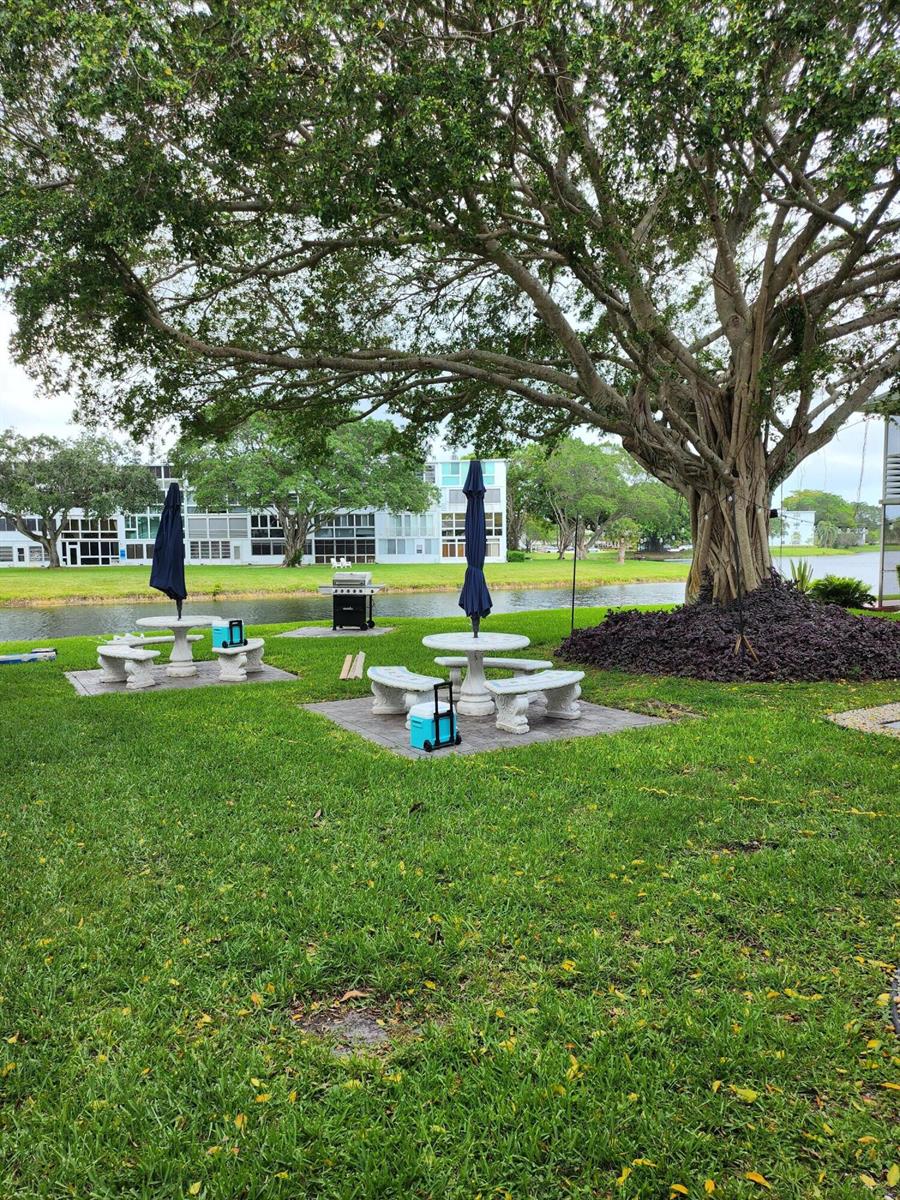 Two outdoor stone picnic tables with umbrellas sit on a grassy lawn near a lake — 168 Durham # 168, Deerfield Beach FL 33442, DEERFIELD BEACH, FL