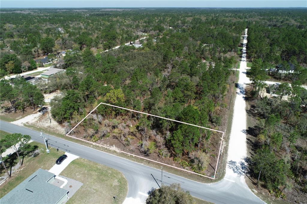 An aerial view shows a rectangular, wooded vacant lot situated at a road intersection — 11283 WOOD OWL AVENUE, WEEKI WACHEE, FL