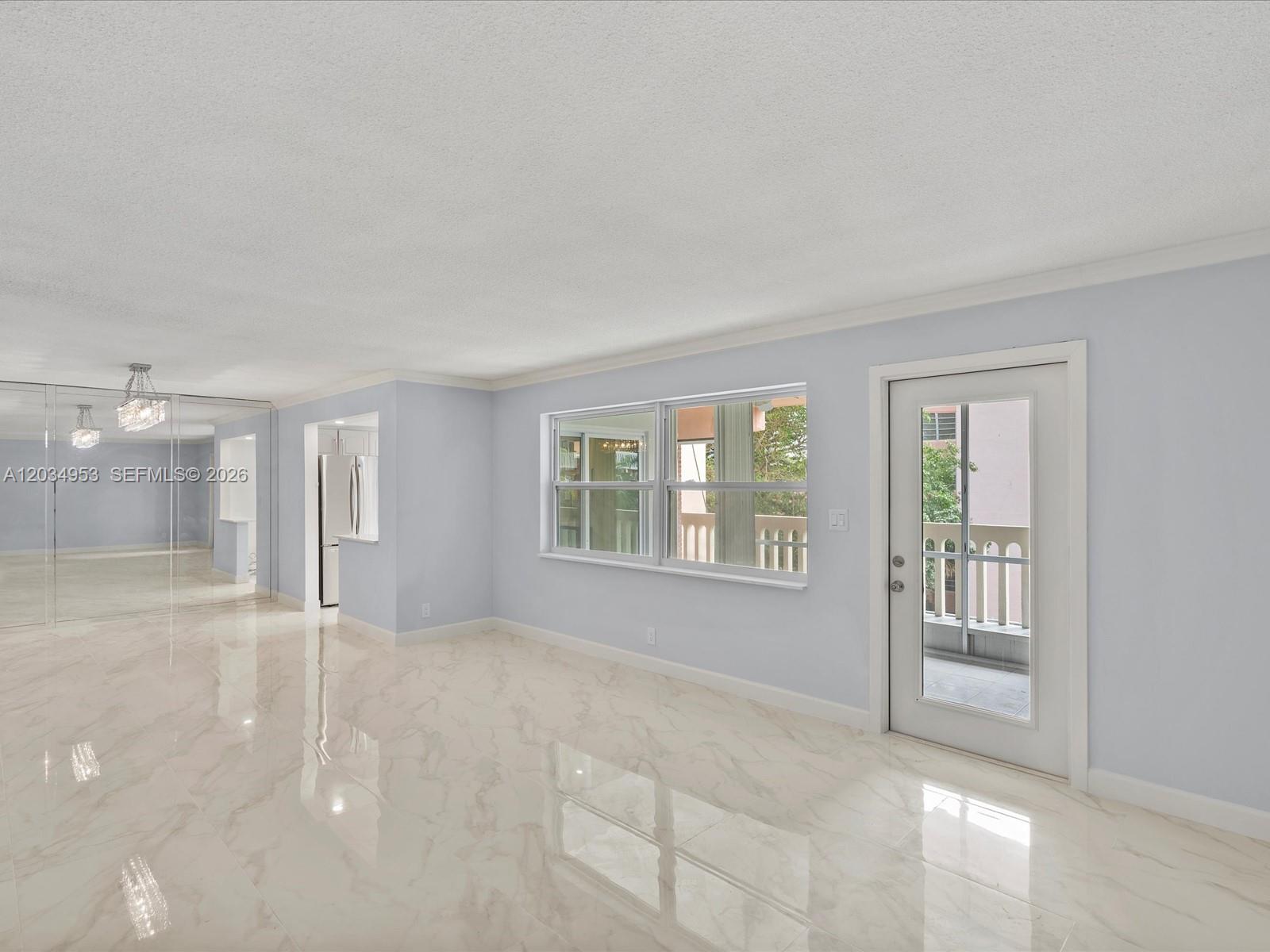 A bright living room features light blue walls, marble-look tile flooring, and a glass balcony door — 200 NE 12th Ave # 7C, Hallandale Beach FL 33009, HALLANDALE BEACH, FL