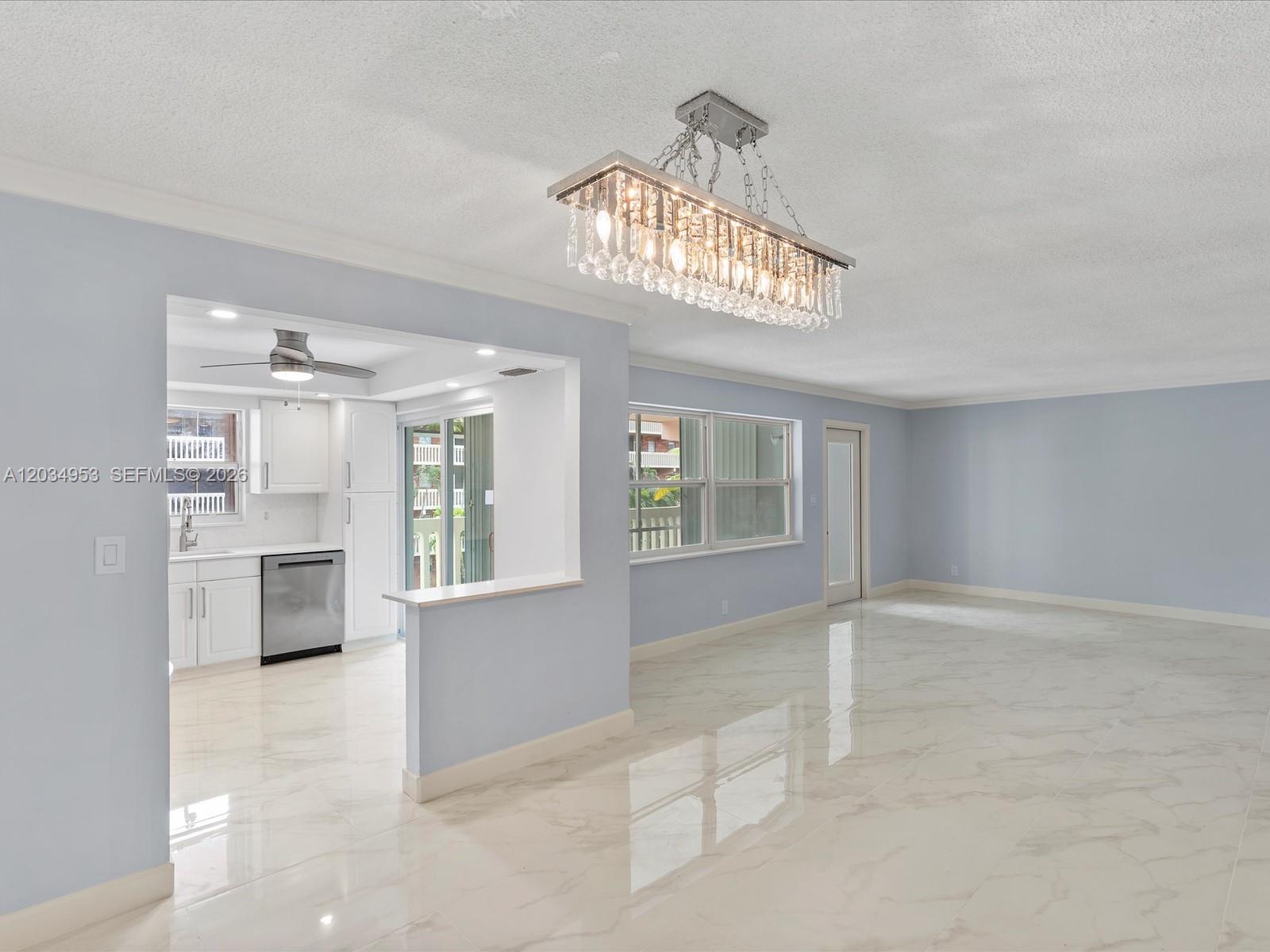 An open-concept living area features light blue walls, white marble-look tile flooring, and a crystal chandelier — 200 NE 12th Ave # 7C, Hallandale Beach FL 33009, HALLANDALE BEACH, FL