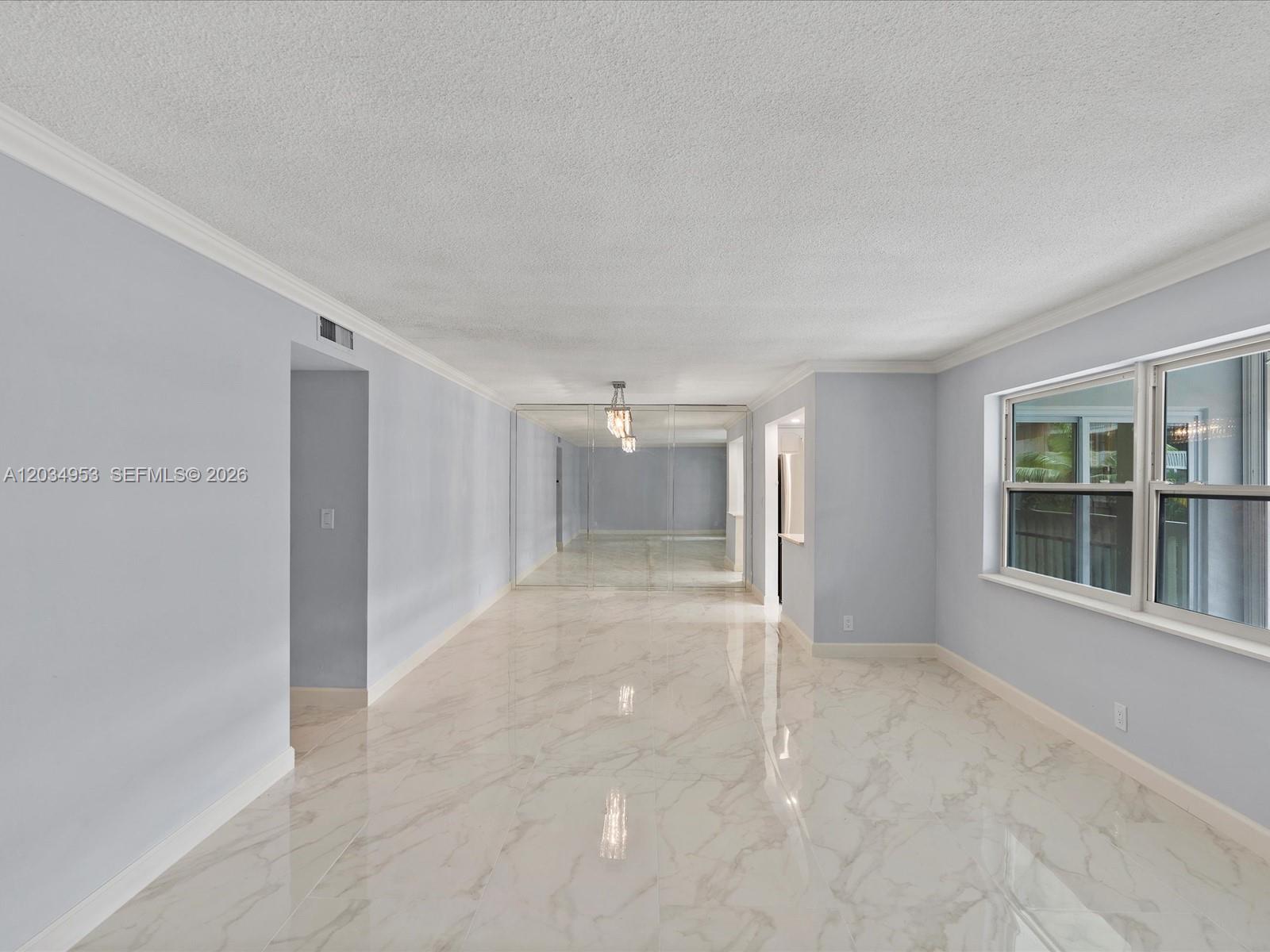 An empty room features light blue walls, white marble-look tile flooring, and a mirrored wall — 200 NE 12th Ave # 7C, Hallandale Beach FL 33009, HALLANDALE BEACH, FL