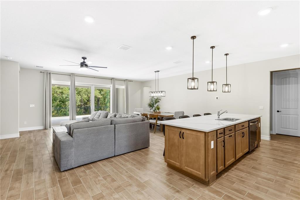 An open-concept living and dining area features a kitchen island, wood-look tile, and sliding doors — 6035 BLUE VIEW WAY, ST CLOUD, FL