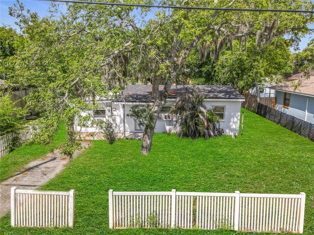 A white single-story house with a large tree in the front yard behind a fence — 1312 JARECKI AVENUE, HOLLY HILL, FL