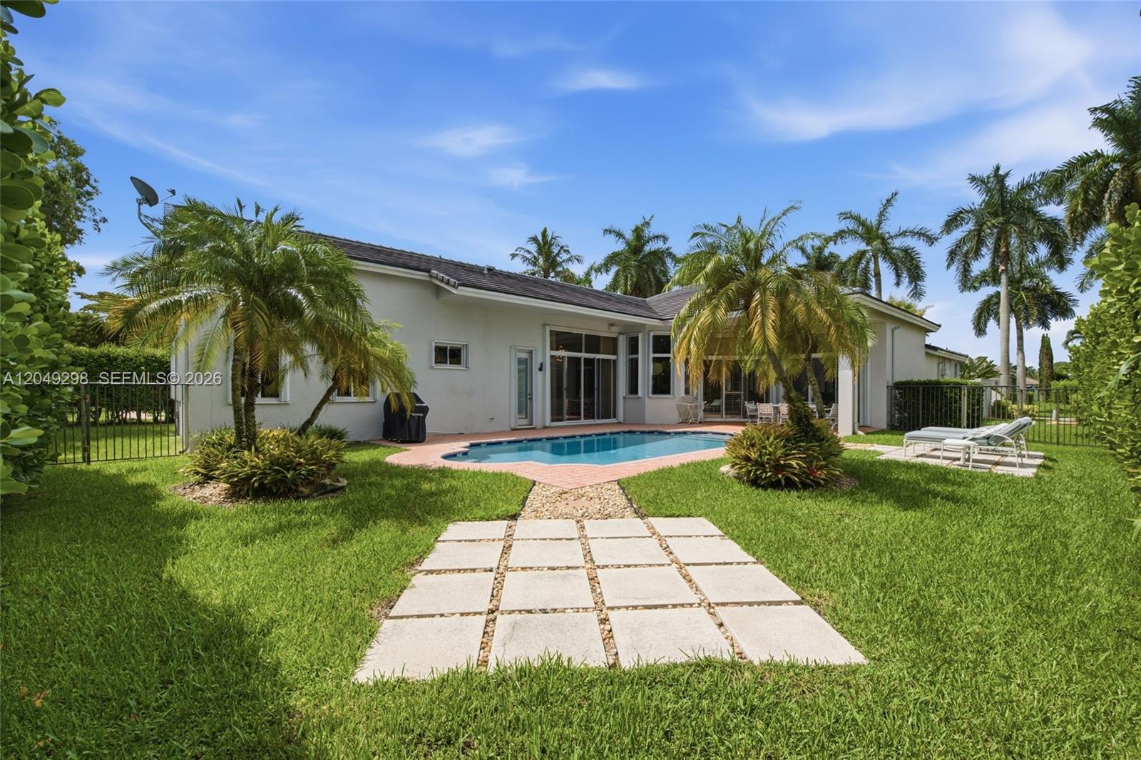 A backyard features a swimming pool, a stone patio, palm trees, and a grassy lawn — 2542 Eagle Run Dr, Weston FL 33327, WESTON, FL